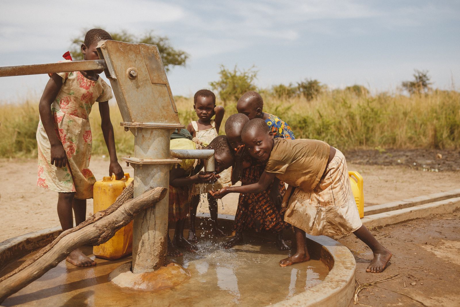 Children gathered around a hand pump, filling containers with water